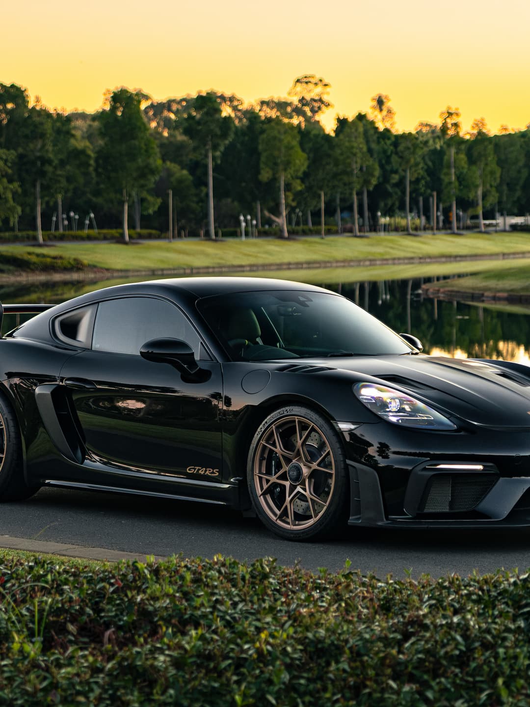 Black Porsche 718 Cayman GT4 RS parked beside a lake at golden hour